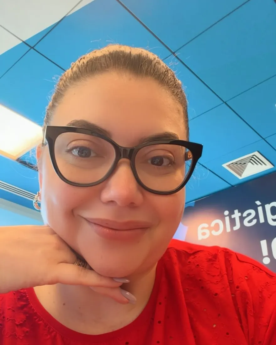 Mayara Schmidt sorri de óculos, com a mão apoiada no queixo
